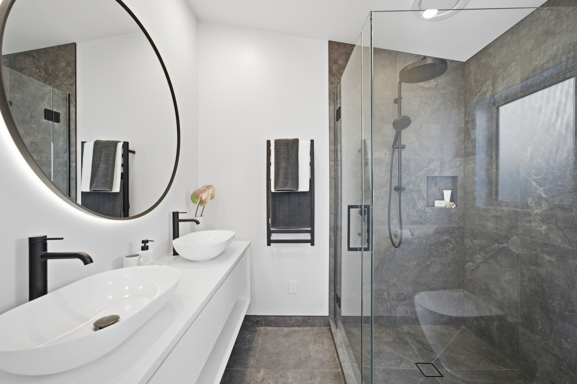 Bathroom with a round backlit mirror, twin basins, and a walk-in shower